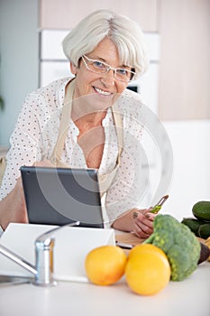 Beautiful senior woman in apron using digital tablet