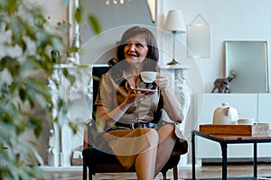 Beautiful Senior Woman Drinking Tea At Living Room and Smiling. Happy Active Life at Any Age. Ageism. Age Shaming