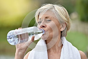 Beautiful senior woman drinking water after excercising photo
