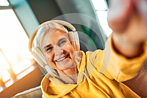 Beautiful senior woman in headphones takes a selfie and smiles at the camera. photo