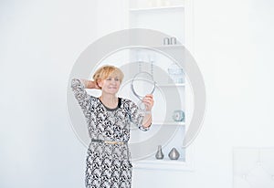 Beautiful senior woman holding hand mirror at white studio