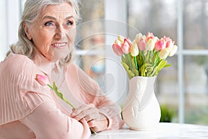 Beautiful senior woman sitting at table with bouquet of tulips