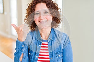 Beautiful senior woman smiling with happy face looking and pointing to the side with thumb up