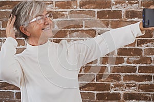 Beautiful senior woman using phone standing against a brick wall smiling
