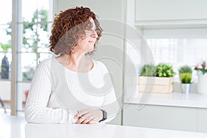 Beautiful senior woman wearing white sweater at home looking to side, relax profile pose with natural face with confident smile