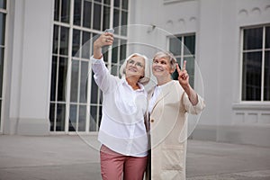 Beautiful Senior women taking selfie photo on mobile phone at city, smile against background of white building. Two