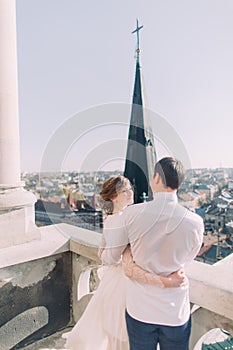 Beautiful sensual blonde bride and handsome groom hugging looking at each other on castle balcony