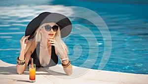 Beautiful sensual blonde with fashionable sunglasses relaxing in the pool with a juice. Attractive long hair woman in black