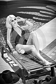 Beautiful sensual blonde with fashionable sunglasses relaxing at swimming pool with a juice. Attractive long fair hair woman