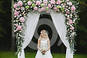 Beautiful and sensual blonde model girl with stylish wedding hairstyle in a white fashionable dress with a bouquet of