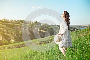 Beautiful sensual brunette in dress and hat standing with eyes closed in nature in bright back lit