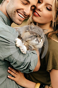 Beautiful sensual couple hug together with the cat and smile cheerfully in nature