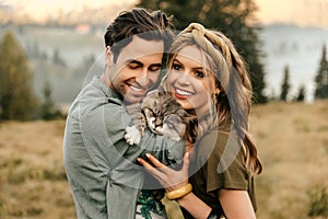 Beautiful sensual couple hug together with the cat and smile cheerfully in nature