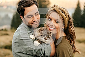 Beautiful sensual couple hug together with the cat and smile cheerfully in nature