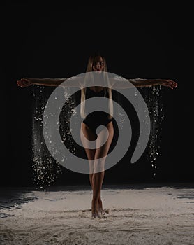 Beautiful sensual slim dancer throwing dust, flour, powder on black background.