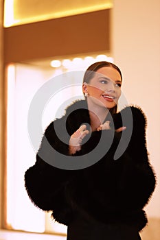 beautiful sensual woman with dark hair in luxurious black fur coat and jewelry posing in hall of the hotel