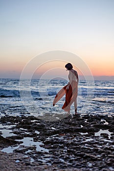 beautiful sensual woman in a red long dress posing on the seashore during sunset. beautiful sunset photo