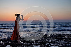 beautiful sensual woman in a red long dress posing on the seashore during sunset. beautiful sunset photo