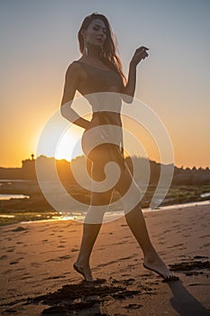 Beautiful sensual woman in sparkling swimsuit at the black sand beach during sunset