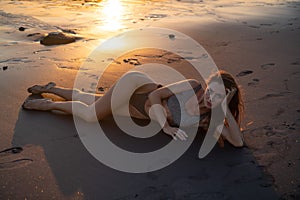 Beautiful sensual woman in sparkling swimsuit at the black sand beach during sunset