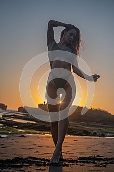 Beautiful sensual woman in sparkling swimsuit at the black sand beach during sunset