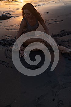 Beautiful sensual woman in sparkling swimsuit at the black sand beach during sunset