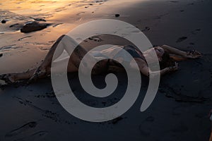 Beautiful sensual woman in sparkling swimsuit at the black sand beach during sunset