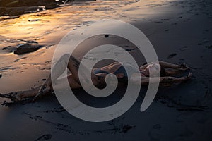 Beautiful sensual woman in sparkling swimsuit at the black sand beach during sunset