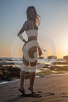 Beautiful sensual woman in sparkling swimsuit posing at the beach over rocks background