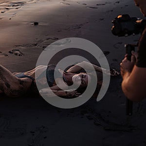 Beautiful sensual woman in swimsuit posing for the videogrpaher at the black sand beach during sunset