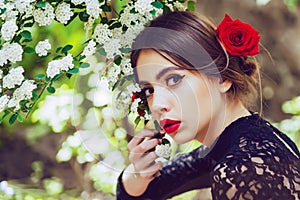 Beautiful sensual young spanish woman in flowers in summer blossom park. Cute girl with red lips posing with white