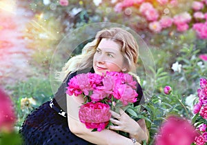 Beautiful and serene young woman hugging a bright bouquet of pink peonies