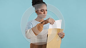 Beautiful serious casual african american girl intently opening envelope with exams results over colorful background