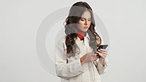 Beautiful serious girl intently using smartphone over white background