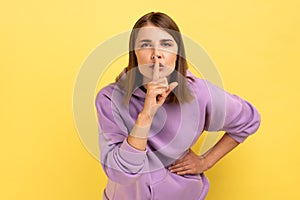 Beautiful serious woman showing gesture secret sign with finger near her lips.