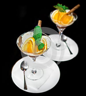 Beautiful serving of scoops of ice cream with slices of orange and mint, ice cream in a glass and saucer with a spoon on a black