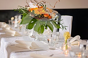 Beautiful set table with a white tablecloth and tableware like cutlery, glasses and napkins. Big flower arrangement in a glass