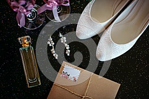 Beautiful set of wedding accessories bride. Morning bride`s. White shoes, pearl earrings, and perfume on a shiny black surface