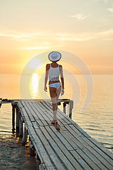 Beautiful sexual woman in white hat and bikini on a wooden pier