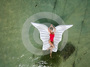 Beautiful and sexy, attractive woman in red swimsuit lays on wing shaped inflatable air mattress floating on water. photo