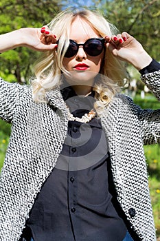 Beautiful blond girl with red lips in sunglasses walking in the garden of a bright sunny day