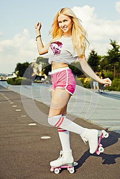 Beautiful blonde girl posing on a vintage roller skates in pink shorts and white T-shirt in the skate park on a warm summer e