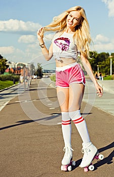 Beautiful blonde girl posing on a vintage roller skates in pink shorts and white T-shirt in the skate park on a warm summer e