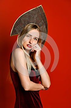 Beautiful sexy blonde Russian girl in traditional kokoshnik hat, velvet festive dress on a red background,