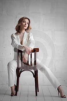 Beautiful sexy blonde in a white unbuttoned suit and underwear, posing sitting on a chair in the studio. Advertising