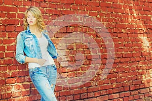 Beautiful blonde woman standing near a brick wall in a denim jacket and pants