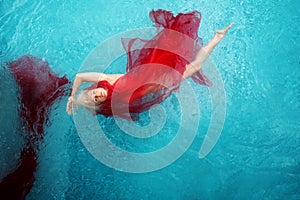Beautiful sexy blonde young woman swimming with red cloths wrapped in turquoise blue pool water, copy space