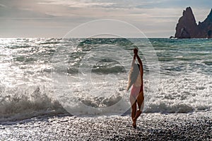 A beautiful and sexy brunette in a red swimsuit on a pebble beach, Running along the shore in the foam of the waves