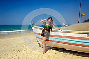 Beautiful sexy brunette on tropical sandy beach near wooden boat on blue sea background and clear sky on hot sunny day