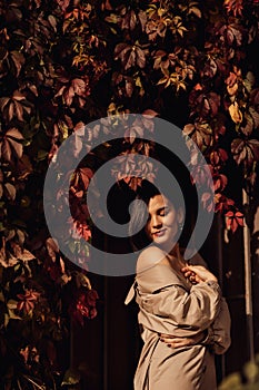 a beautiful sexy brunette woman in a coat by the hedge braided with autumn vines